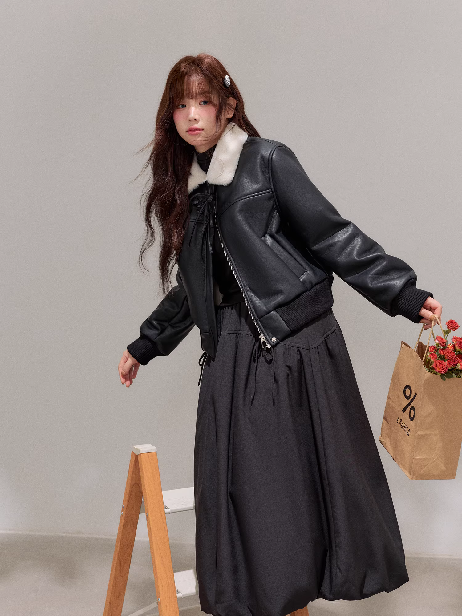 Bộ trang phục mùa đông cho nữ cỡ lớn: Áo khoác da đen tôn dáng với cổ lông trắng và bộ chân váy hoa lưng cao.